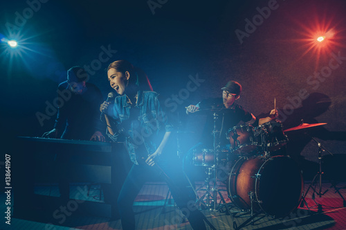 Musician band hand holding the microphone and singing a song and playing music instrument with Fellow band musicians on black background with spot light and lens flare  musical concept