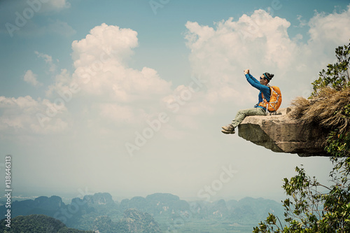 successful woman hiker taking photo with smartphone on mountain peak cliff
