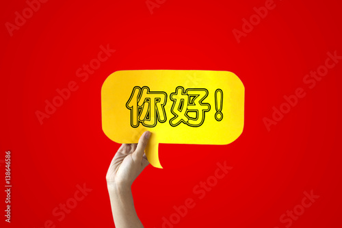 Human Hands Holding 'Nihao' Yellow Speech Bubble Over Red Background - Chinese language learning concept photo