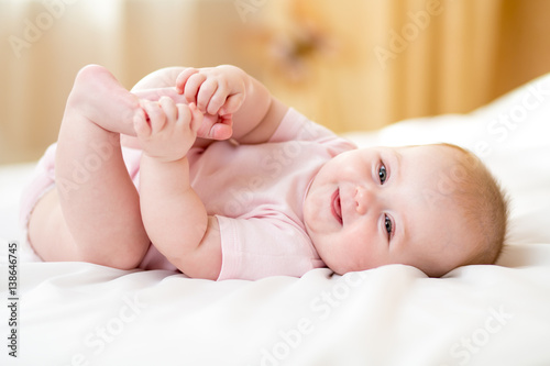 happy baby girl lying on white sheet and holding her legs