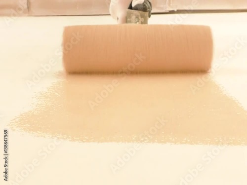 Worker's hand with roller puts paint on the wall.