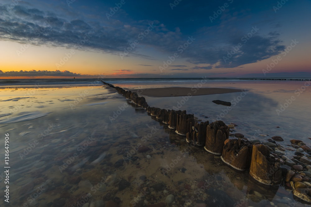 Baltic sea at beautiful sunrise,wooden breakwater in the light of the setting sun