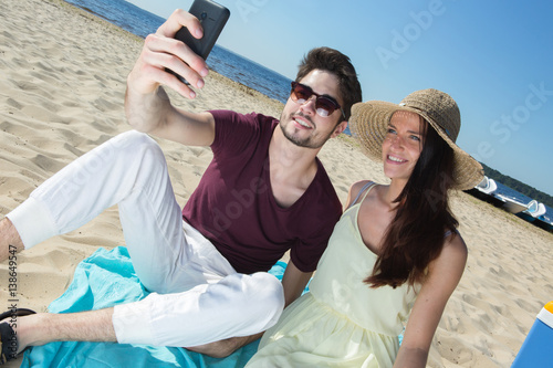 gorgeous young couple sitting at the beach and doing selfie