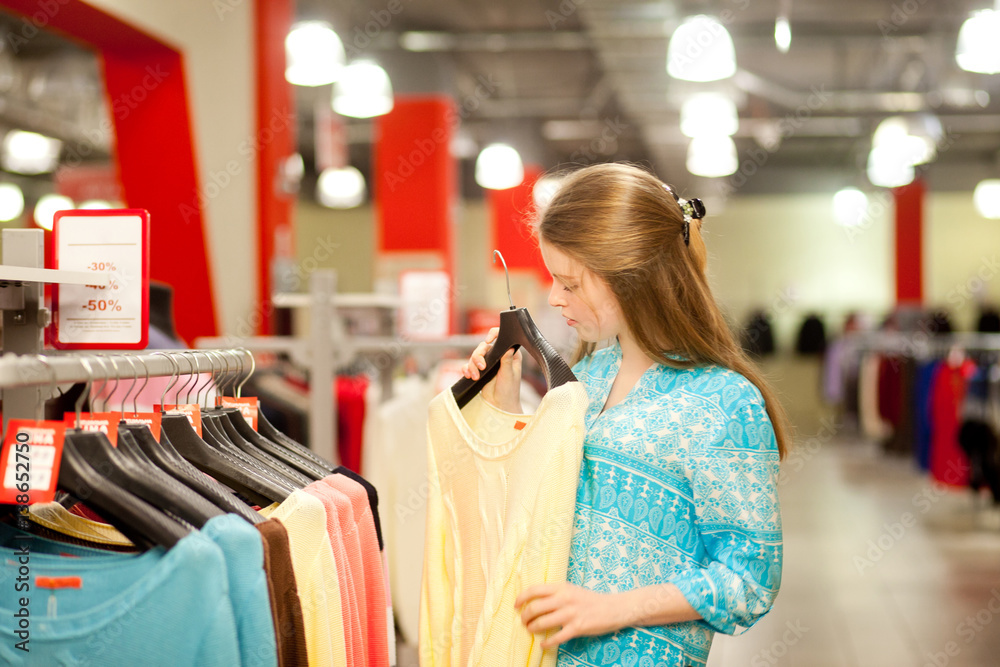Young woman chooses clothes and looks in the boutique, shopping center or store, shopping