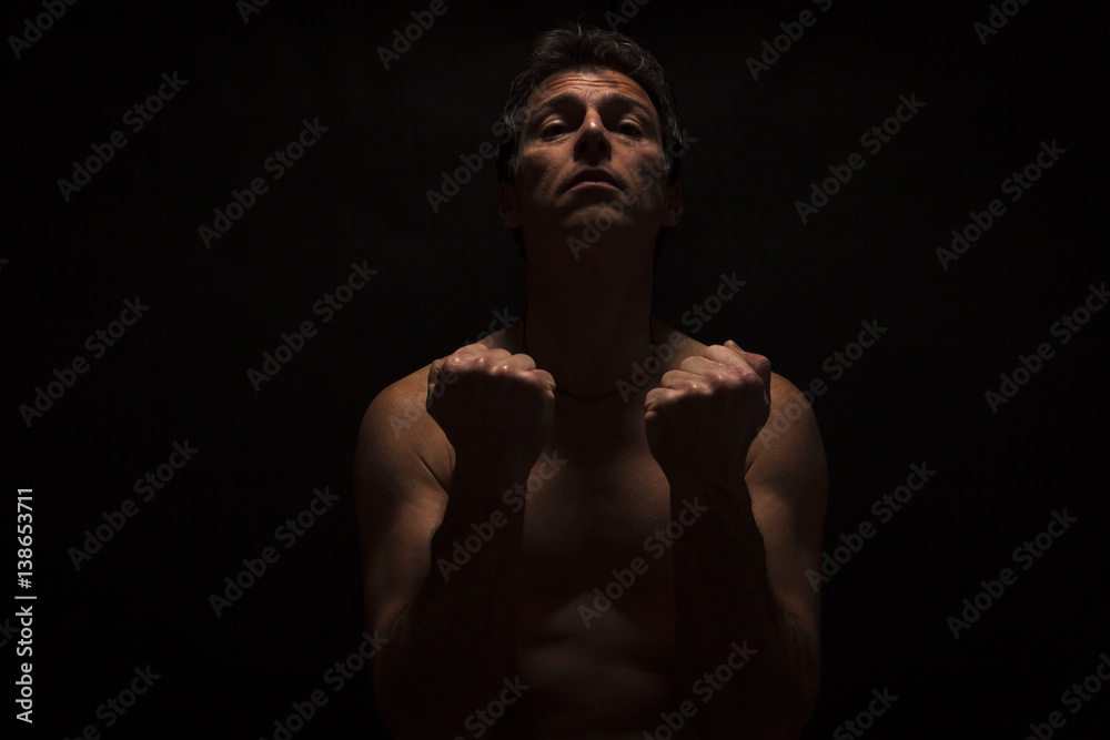 Low key portrait of shirtless caucasian man with fists. Black background