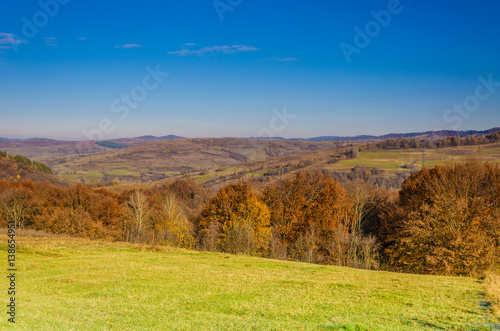 Autumn landscape  trees with colorful leaves  frost on green grass  autumn mountain in fog in the background.