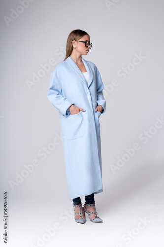 Fashionable blonde in a light blue coat. Photography in full height in a studio on a gray background