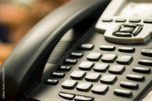 businessman dialing voip phone in the office, keyboard and monitor detail in the background with vintage color tone effect