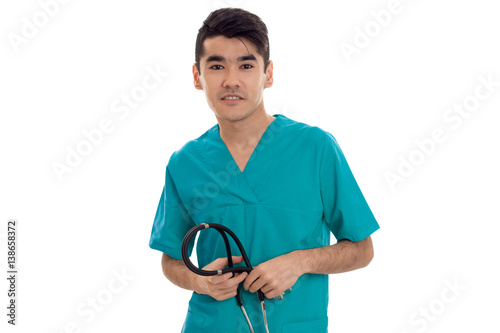 Cute young man doctor in blue uniform with stethoscop in his hands posing and looking at the camera isolated on white background