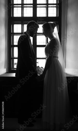 Silhouettes of wedding couple hugging at old ancient room near window. Black and white.