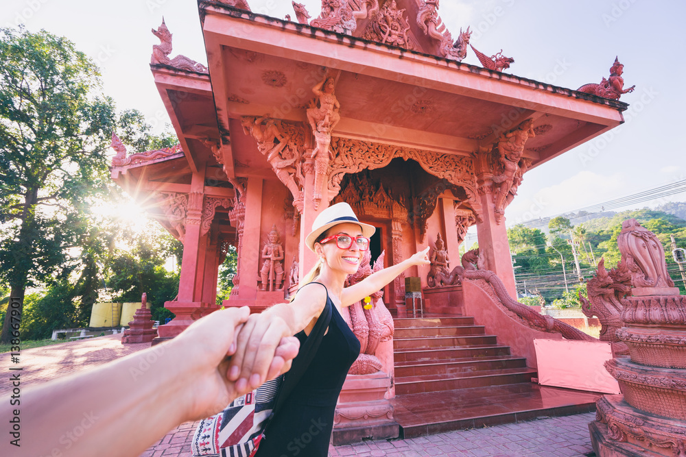 Fototapeta premium Follow me. Travel by Asia. Young woman holding boyfriend's hand showing temple on Samui Island in Thailand.