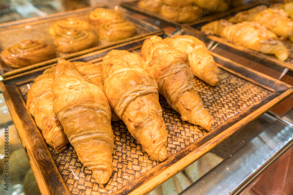 fresh croissants lying on wooden tray display in the bakery shop.