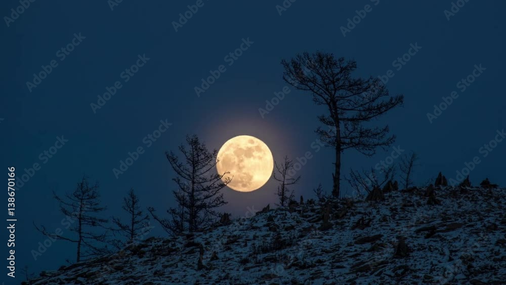 Night Time lapse Large full bright moon rises from above hill into sky.