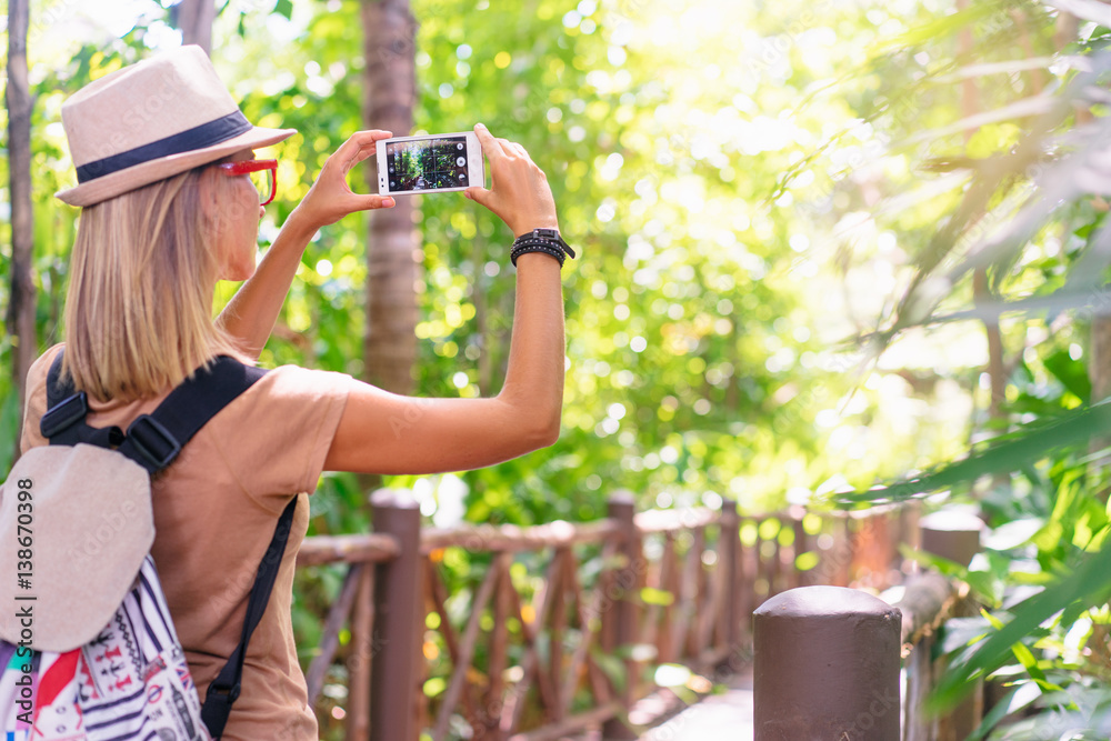 Naklejka premium Travelling concept. Photographing adventure. Young woman taking picture on her smartphone in jungle.