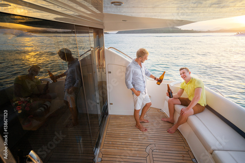 Friendship and vacation. Two young handsome men talking and drinking beer on the yacht sailing the sea.