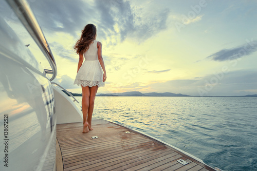 Luxury travel on the yacht. Young woman enjoying the sunset on boat deck sailing the sea. © luengo_ua