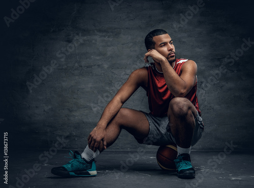 Basketball player sits on a floor and holds a ball.