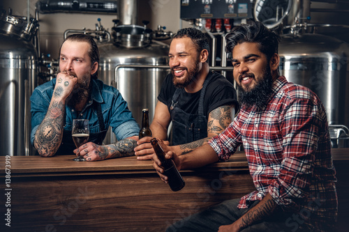 Stylish three men drinking craft beer in the microbrewery.