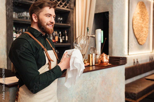 Young bearded man bartender standing in cafe.