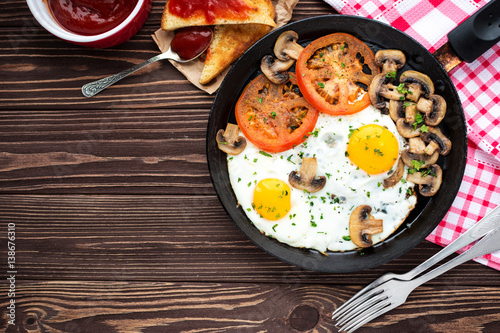 Fried eggs with mushrooms and tomato on dark wooden table