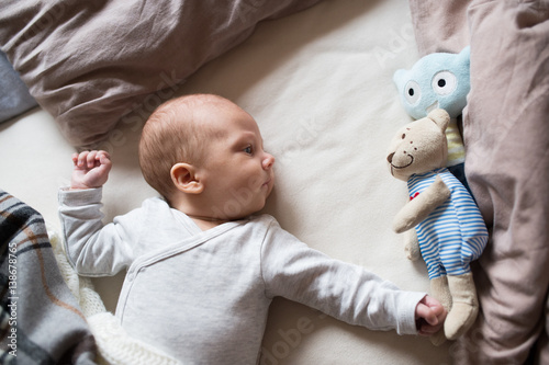 Cute newborn baby boy with teddy bear lying on bed