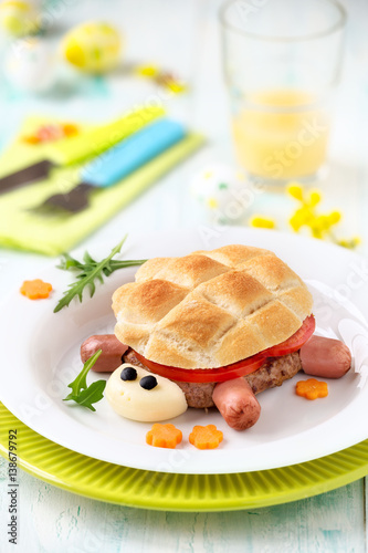 Fun food for kids - cute turtle shaped hamburger made of ground meat pattie, slices of fresh tomato and bread with Easter decoraions at the background photo