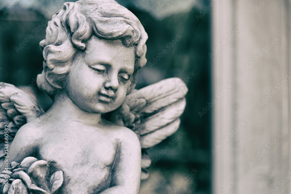 Obraz premium Beauty Cupid statue of Angel in vintage garden on summer. Holding bouquet flowers in his hand