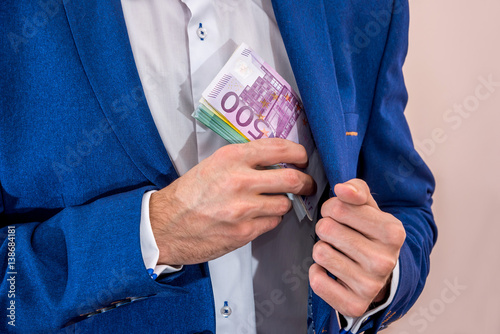 Businessman removing 500 euro banknotes from his jacket pocket.