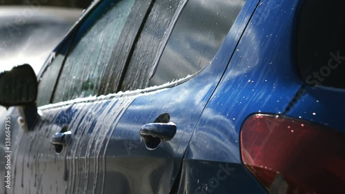 Blue car washed by hand using a water jet wash in a shiny day