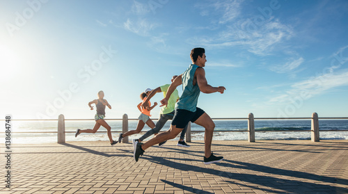 Fototapeta Naklejka Na Ścianę i Meble -  Young runners sprinting on the ocean front path