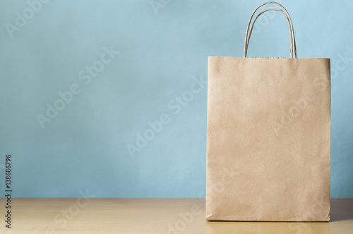 Blank Brown Carrier Bag with Handles on Light Wood Veneer Table with Blue Background