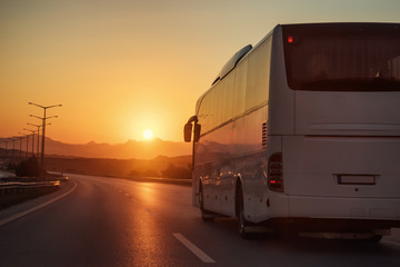 White bus driving on road towards the setting sun