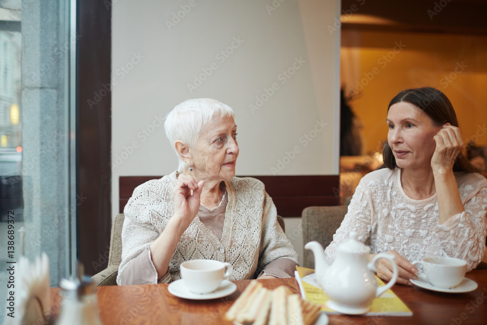 Senior friendly women sitting in armchairs and talking in cafe