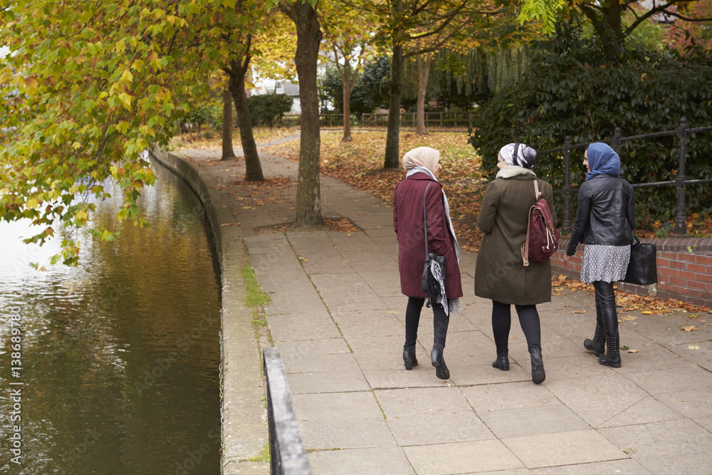 British Muslim Female Friends Walking By River In City British Muslim Female Friends Walking By River In City