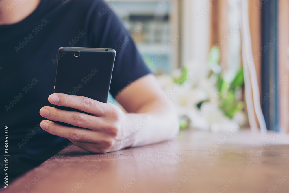 A man holing and using on black smart phone in modern cafe A man holing and using on black smart phone in modern cafe