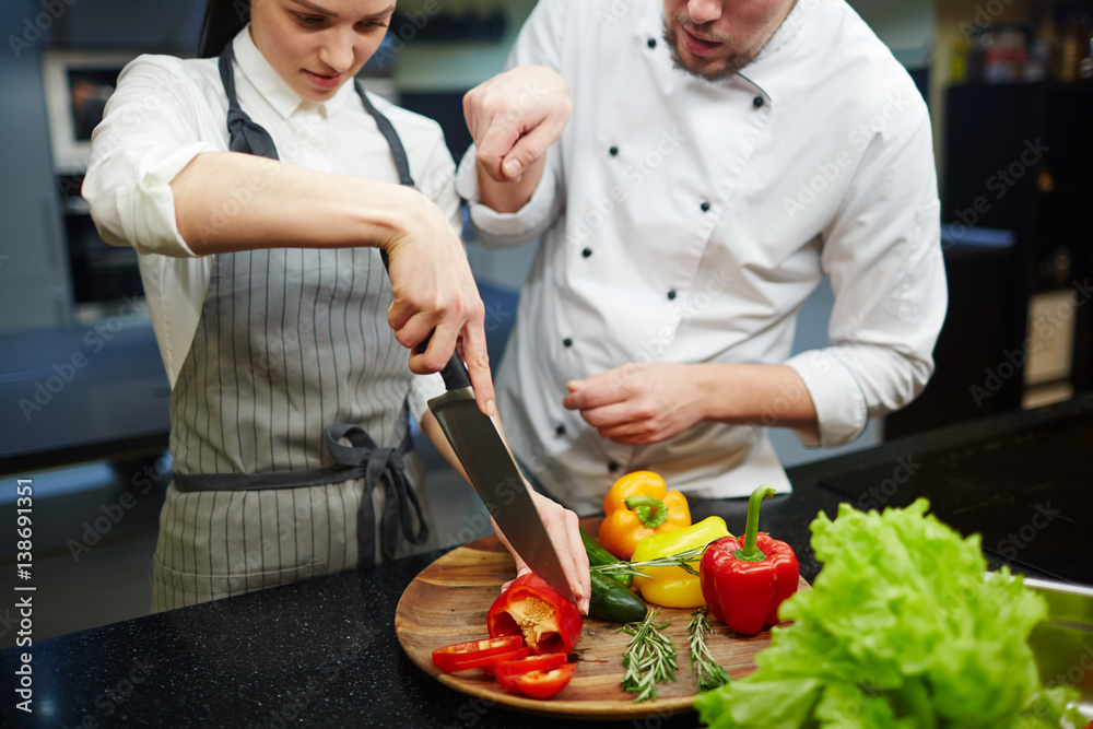Young woman cutting fresh pepper with chef near by Young woman cutting fresh pepper with chef near by