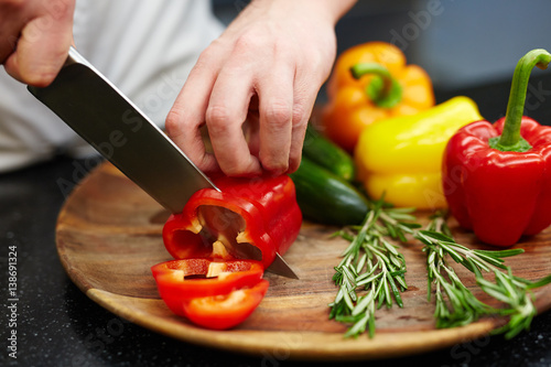 Chef cutting red pepper on wooden board