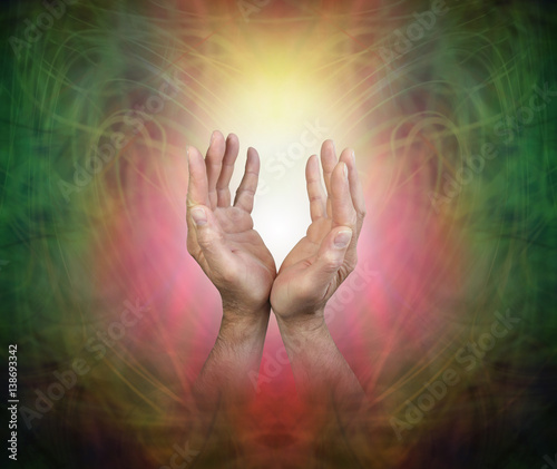 Male hands sensing Pranic Energy Field - male hands reaching up into a golden orb light on a beautiful ethereal green and red  vignette pattern background with copy space
