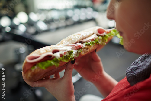 Closeup shot of big greasy fattening sandwich in hands of overweight woman