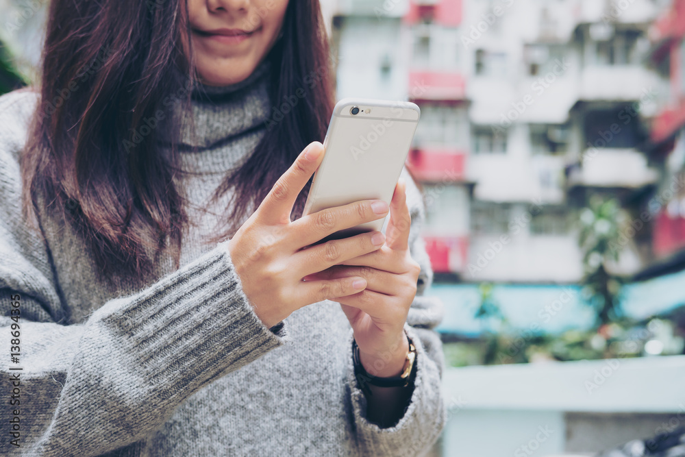 Beautiful girl with smiley face holding and using smart phone with flat building background Beautiful girl with smiley face holding and using smart phone with flat building background