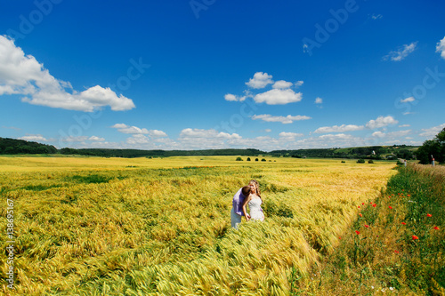 Look from afar at groom kissing bride's shoulder while wind blows wheat on field