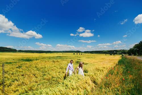 Bride and groom walk across field of wheat under deep blue sky