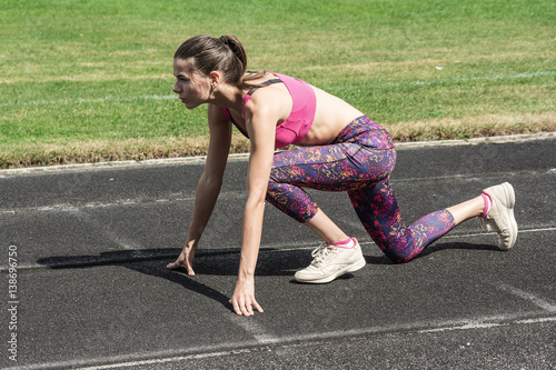 Young woman athlete at starting position ready to start a race. Female sprinter ready for sports exercise on racetrack