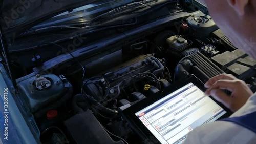Mechanic in a auto repair shop checking engine using a digital tablet