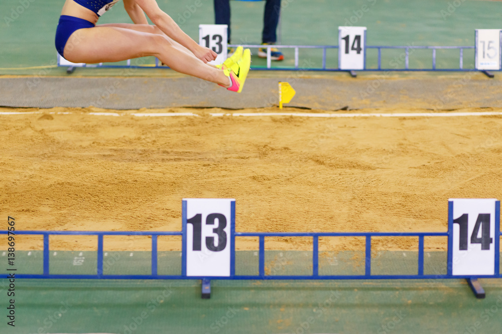 Sportswoman jumping into sandpit on triple jump competition in track