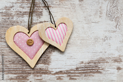 two pink colored wooden hearts on white wooden background