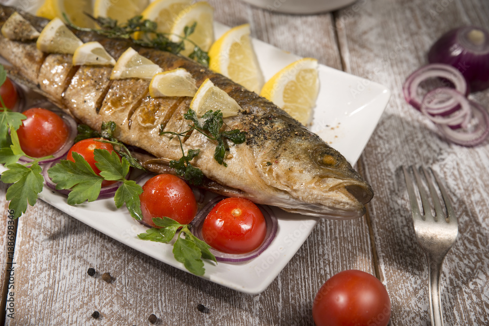 healthy food: two fried sea bass fish served with tomatoes and vegetables on big wooden board over table healthy food: two fried sea bass fish served with tomatoes and vegetables on big wooden board over table