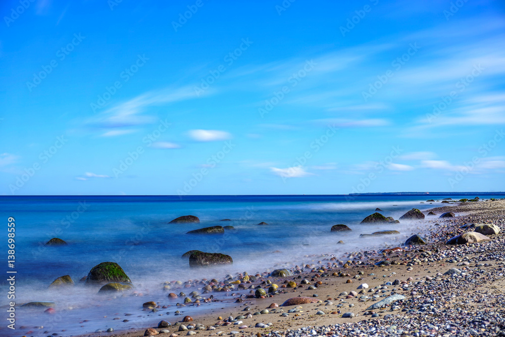 Langzeitbelichtung Strand mit Steinen und blauem Himmel