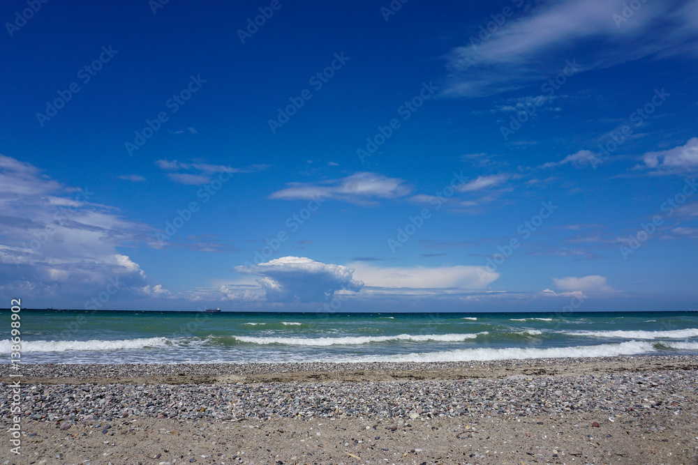 weiter Strand mit Steinen, Meer und blauem Himmel