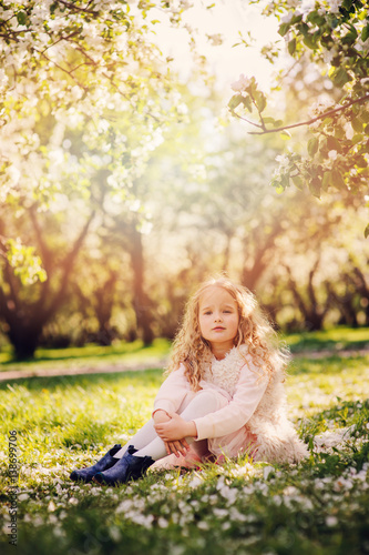 spring portrait of beautiful child girl with curly long hair walking outdoor in blooming garden